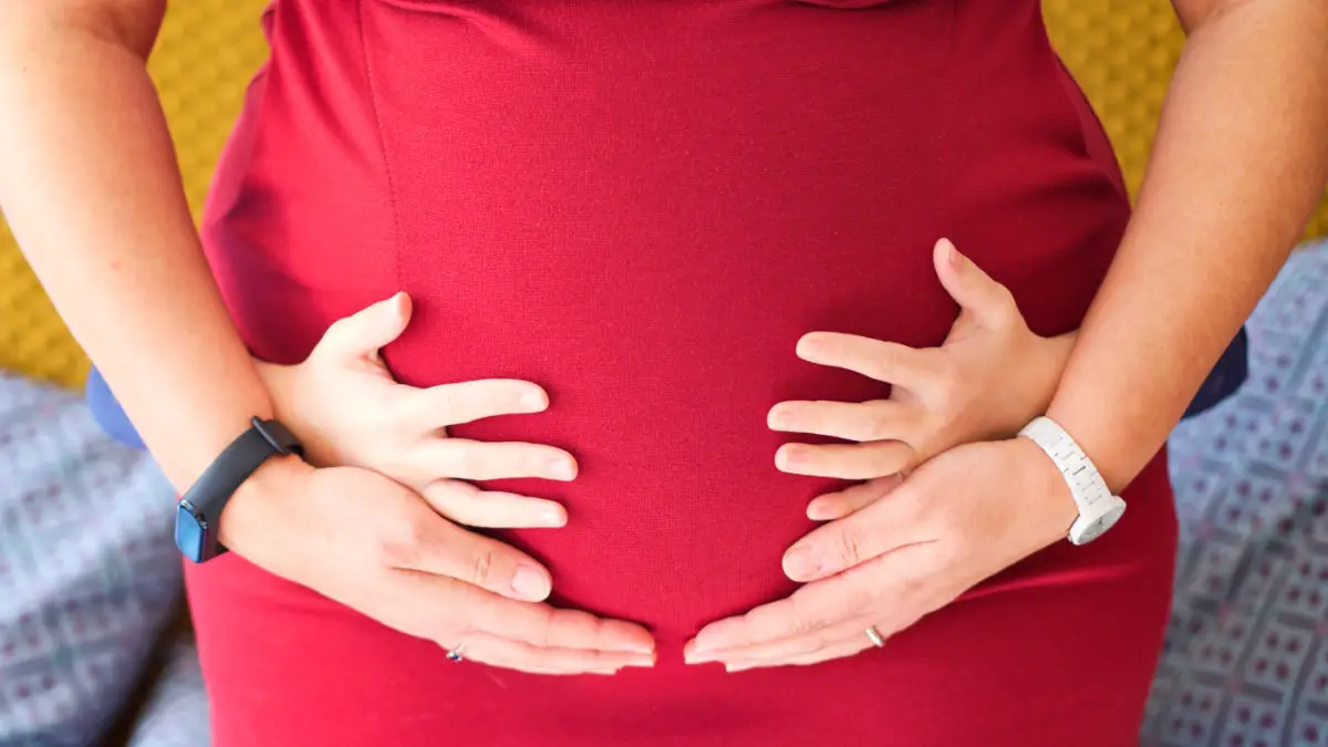 Kinderhände am Babybauch - rotes Kleid - Schwanger trotz Endometriose